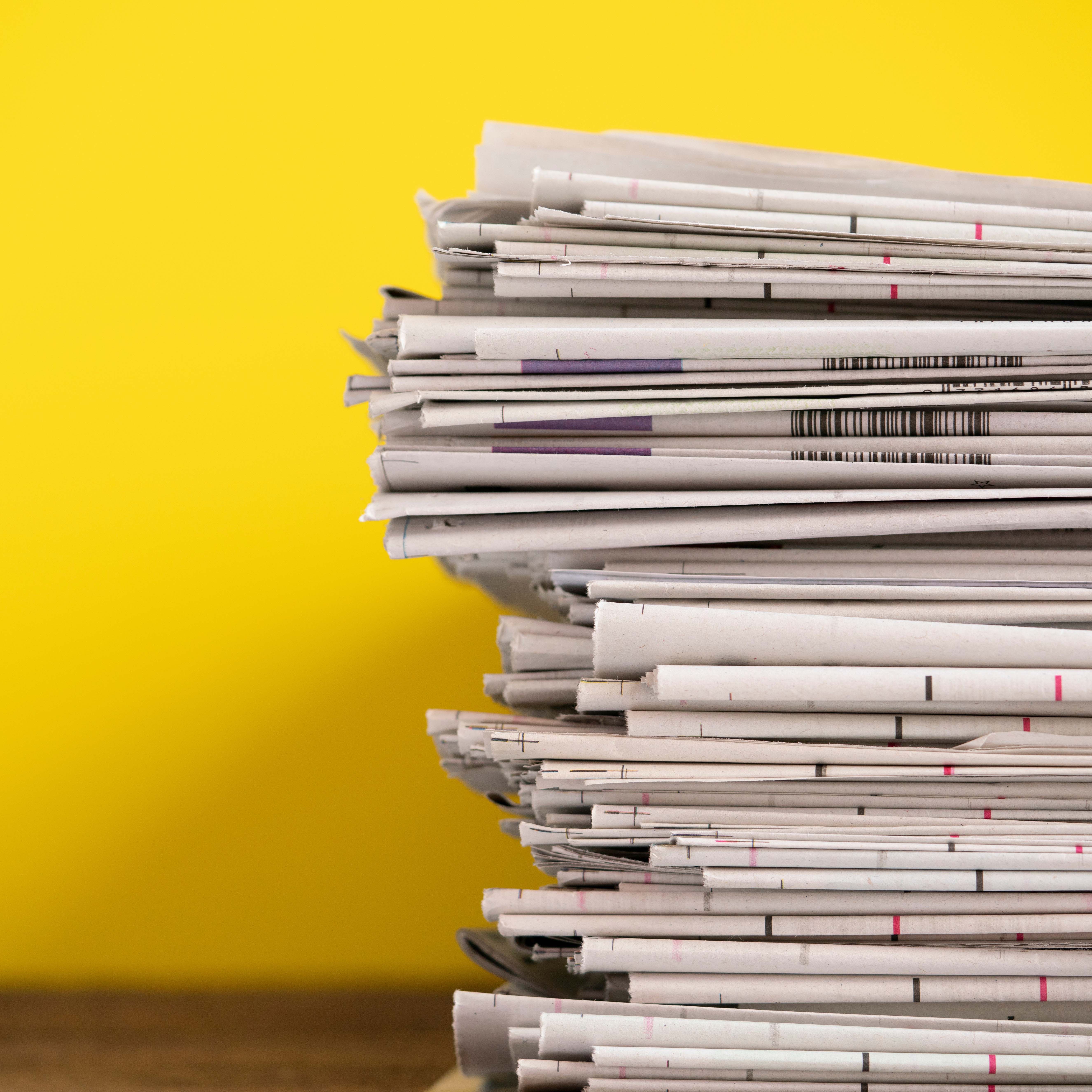 close up newspapers folded and stacked on yellow background on t